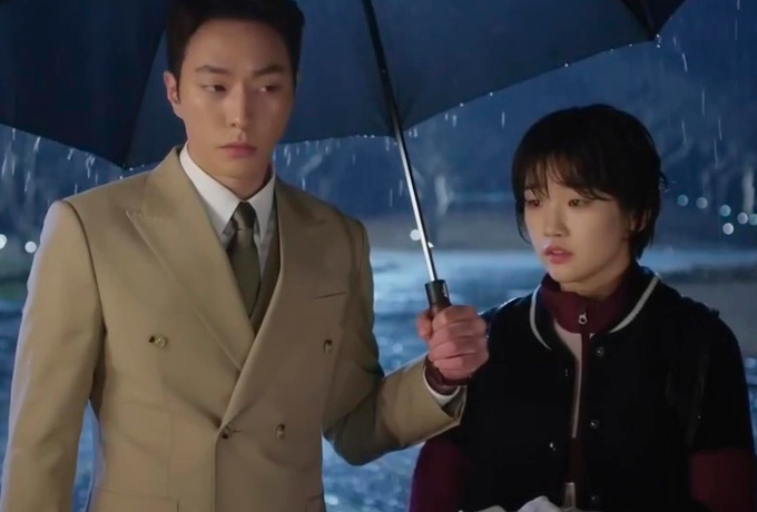 Lee Yoon-sung de terno segurando um guarda chuva para Ha-won, que usa uniforme da escola.